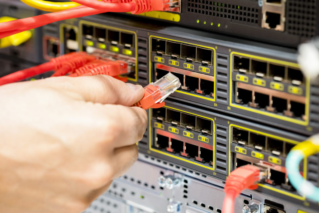 Closeup of technicians hand plugging fiber cable into switch in datacenter