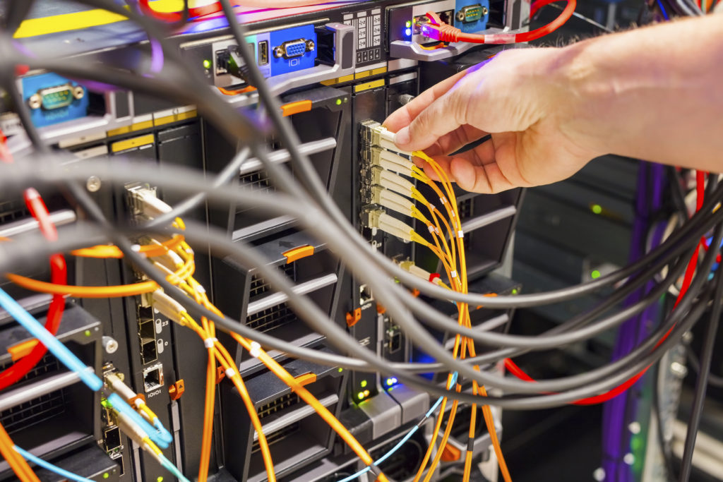 Closeup of IT technician's hand plugging fiber channel cable into switch in datacenter